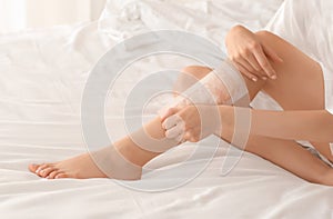 Young woman epilating her legs with wax on bed