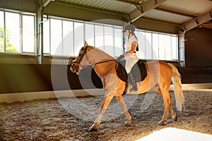 Young woman in equestrian suit riding horse indoors. Beautiful pet