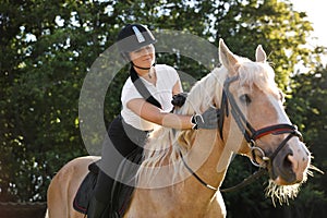 Young woman in equestrian suit riding horse outdoors on sunny day. Beautiful pet