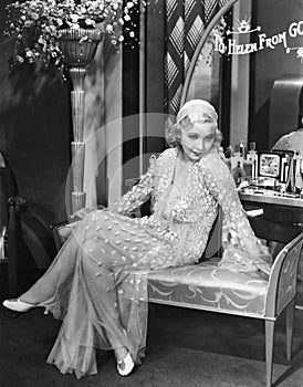 Young woman in an evening gown sitting on an upholstered bench