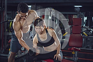 Young woman exercise in a gym with the help of her personal trainer, Fitness instructor exercising with his client at the gym