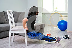 Young woman exercise at home. Sporty healthy lifestyle. Woman using a chair while doing workout