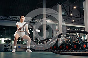 Young woman exercising with battle rope at the gym