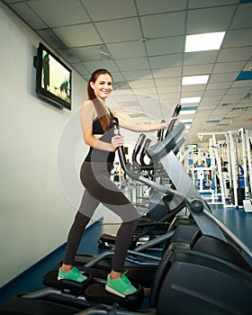 Young woman exercising on cardio machines in gym