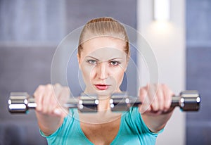 Young woman exercising with dumbbells at the gym training shoulders