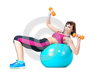 Young woman exercising with dumbbells laying on a fitness ball