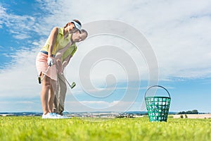 Young woman exercising the golf swing helped by her instructor