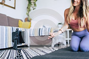 Young woman exercising at home doing workout and recording at her with cellular phone to teach workout and produce web class