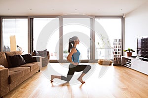 Young woman exercising at home, stretching legs.