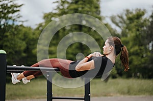 Young woman exercising outdoors, doing a horizontal bar workout in a park