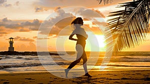 Young woman exercising running barefoot on sea beach with sunset ocean background. Female athlete silhouette cardio