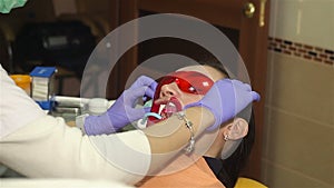 Young woman with an expander in mouth at the dental clinic. Application of protective whitening gel to the teeth.