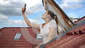 Young woman experiences signal issues with her cellphone as she peers out of an open attic window, attempting to regain