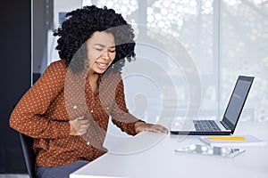 Young woman experiencing stomach ache while working at office