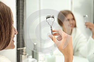 Young woman with eyelash curler near mirror in bathroom