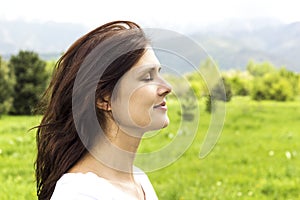 Young woman with eyes closed breathing deeply fresh air in the mountains.