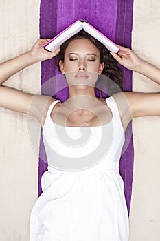 Young woman with eyes closed holding book while lying on picnic blanket