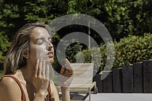 Young woman with eyes closed putting and spreading white sun cream on her face befo entering the water in the pool photo