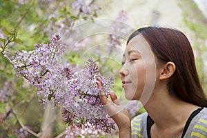 Young woman with eyes closed smelling a flower blossom in the park in springtime