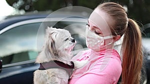 A young woman in a fabric face mask holding her little dog. Covering face in public is recommended by CDC in many