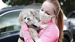 A young woman in a fabric face mask holding her little dog. Covering face in public is recommended by CDC in many