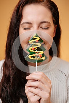 Young woman face close-up with sweet lollipop by Christmas tree.