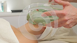 Young woman with face covered with green moisturizing alginate mask in beauty salon. Applying a cosmetic mask