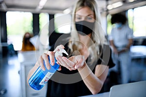 Young woman with face mask back at work in office after lockdown, disinfecting hands. photo