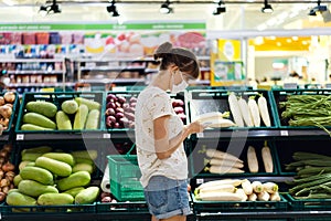 Young woman with face mask using mobile phone and buying groceries in the supermarket