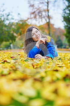 Young woman on a fall day, laying on the ground with colorful autumn leaves