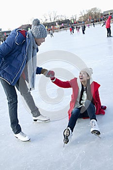 Young woman falls on the ice while skating, boyfriend helps her up