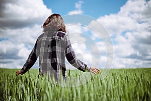 Young woman farmer walks at the green wheat field touching spikelets with her hand. Female farm worker checking the