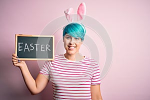 Young woman with fashion blue hair wearing easter rabbit ears and holding blackboard with holiday word with a happy face standing