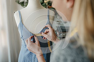 Young woman fashion designer measuring mannequin, seamstress holding tape working with dummy in cozy home or tailor shop,