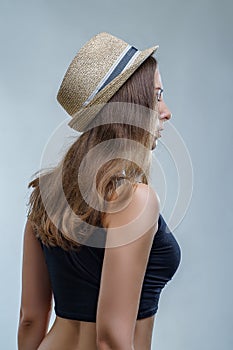 Young woman in fashionable hat and black shirt posing in a half turn from the back on gray background in studio