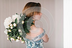 Young woman in fashon dress holding bouquet of beautiful white peonies flowers behind her back St. Valentine`s Day, International