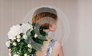 Young woman in fashon dress holding bouquet of beautiful white peonies flowers behind her back St. Valentine`s Day, International