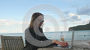 Young woman fast typing on laptop in outdoor cafe