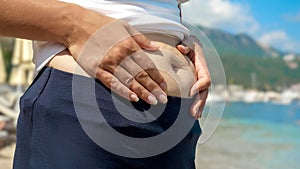 A young woman with fat on belling being shy of her body by the sea beach, confidently standing during her summer holiday