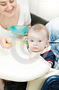 Young woman feeding her baby from spoon with apple sauce