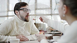 Young woman is feeding her husband with a cake whle sitting in a cafe