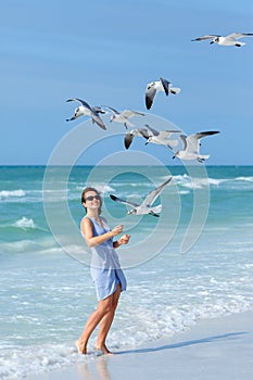 Young woman feeding seagulls on tropical beach photo