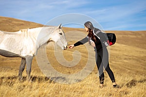 Young woman feeding a wild white horse on a meadow