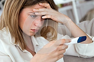 Young woman feeling depressed and sad after looking at pregnancy test result at home.