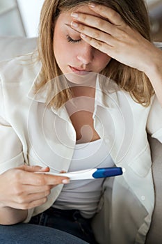 Young woman feeling depressed and sad after looking at pregnancy test result at home.