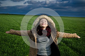 Young woman feeling happy in a green field with clouds enjoying fresh air