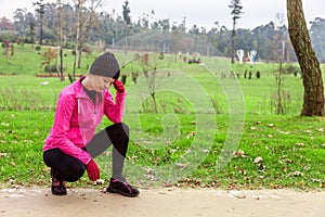 Young woman feeling lightheaded or with headache after train on a cold winter day on the training track of an urban park.