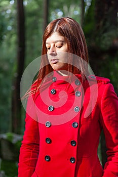 Young woman feeling sad walking alone on forest path wearing red long coat