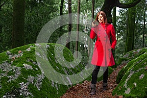 Young woman feeling sad walking alone on forest path wearing red long coat