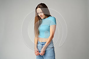 Young woman feeling uncomfortable and shy on gray background